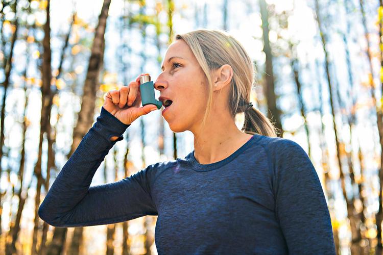 Frau benutzt beim Joggen Asthmaspray