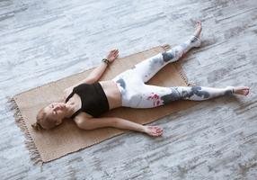 Eine Frau liegt ausgestreckt auf einer Gymnastikmatte, Arme und Beine leicht abgespreizt.