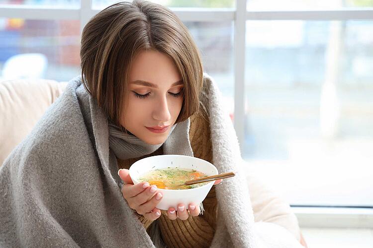 Erkältungsmythen – Frierende Frau wärmt sich die Hände an warmer Suppenschüssel