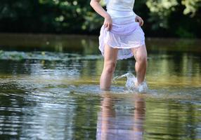 Frau watet mit nackten Füßen durch einen Fluß