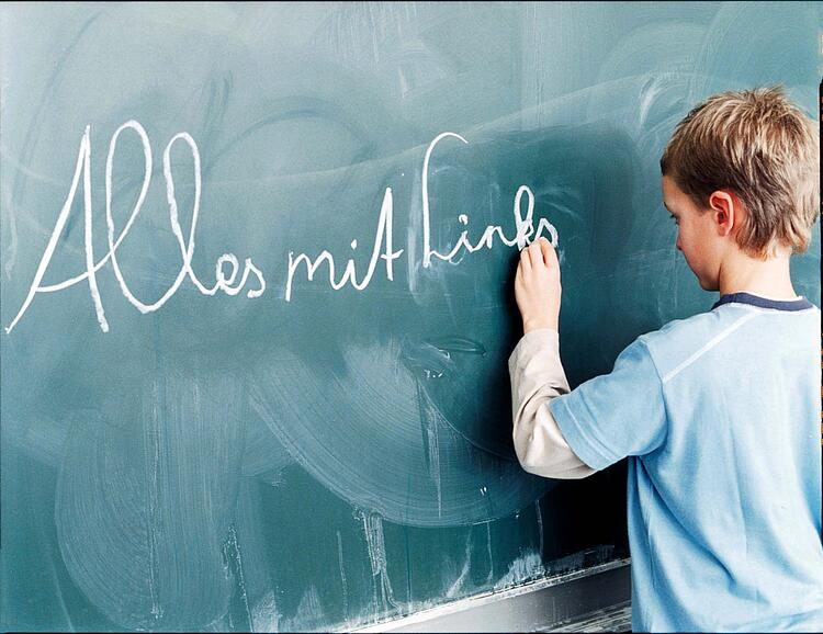 Ein Junge schreibt mit der linken Hand an die Tafel.