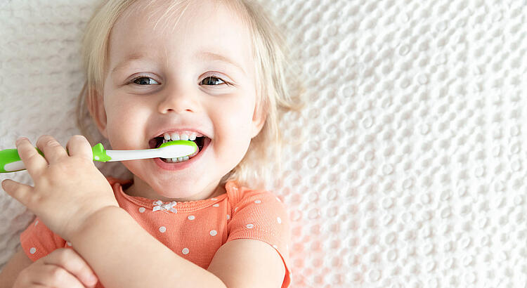 Kleines Mädchen mit Zahnbürste im Mund.