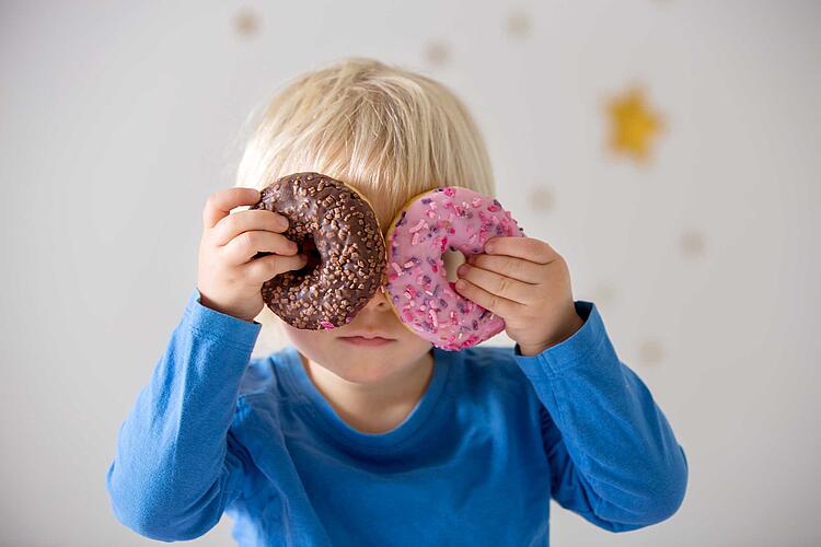 Junge hält sich zwei Donuts vor die Augen.