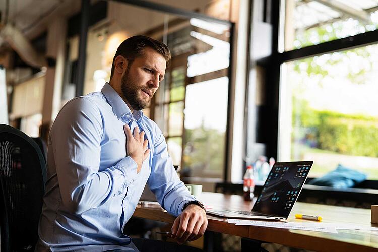 Mann arbeitet am Laptop und greift sich ans Herz