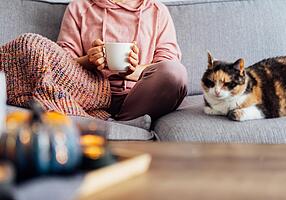 Frau sitzt mit einer Tasse Tee und einer Katze auf dem Sofa