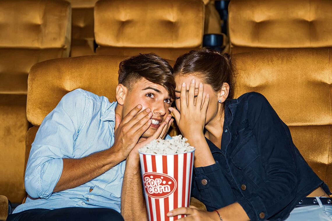Paar im Kino gruselt sich und hält sich die Augen zu.