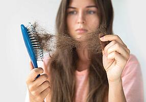 Junge Frau schaut traurig auf ihre Haarbürste voller Haare