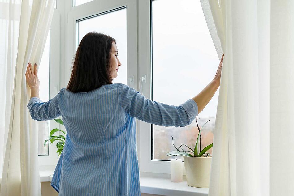 Frau öffnet die Gardinen am Fenster