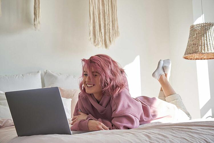Weiblicher Teenager leigt auf dem Bett und schaut auf einen Laptop