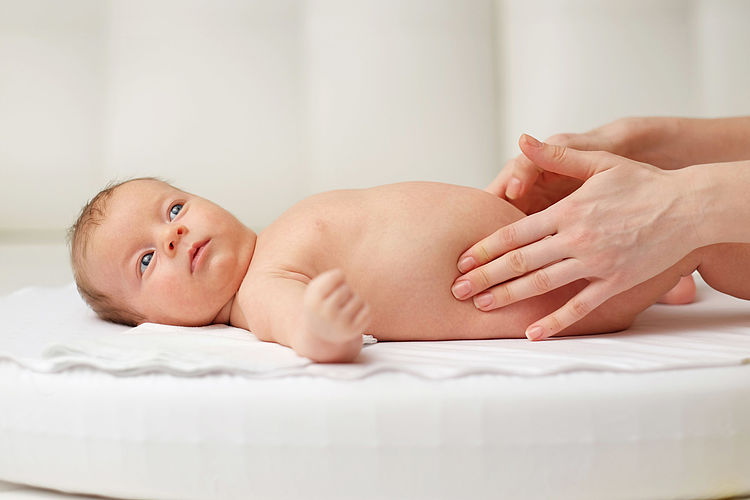 Bildnachweis: © istockphoto.com / haveseen Ein Baby liegt auf dem Rücken und wird von Frauenhänden sanft massiert.
