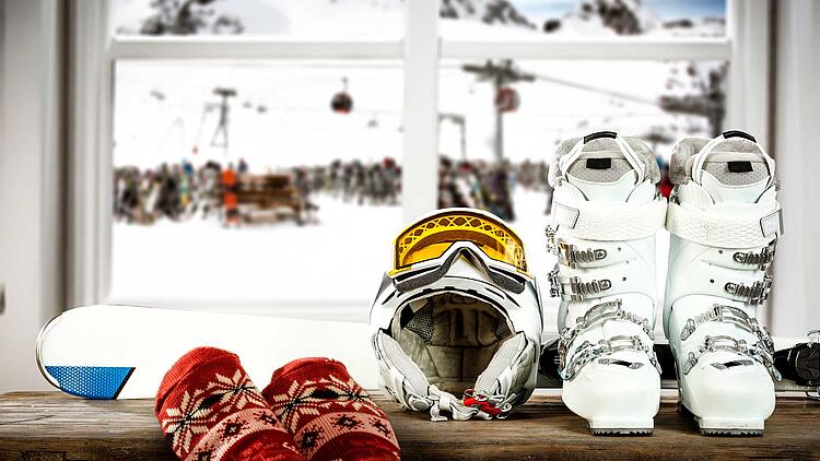 Skier, Skischuhe und Skihelm vor einem Fenster mit Blick auf einen Skilift