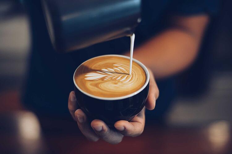 Barista gießt Milch in eine Tassse Kaffee