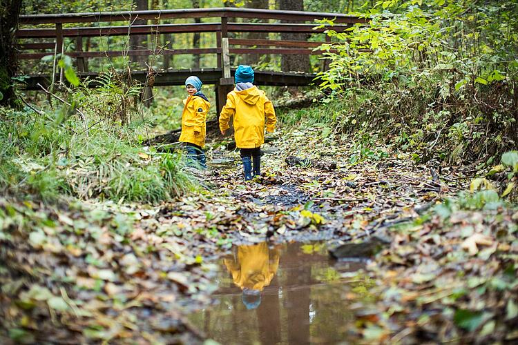 Kinder in gelben Regenmänteln laufen durch einen Bach