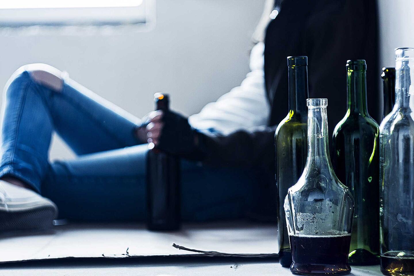 Verschiedene Flaschen stehen auf dem Boden, dahinter sitzt eine Person mit einer Flasche in der Hand