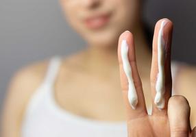 Junge Frau mit genau der richtigen Menge Sonnencreme für Hals und Gesicht auf zwei Fingern