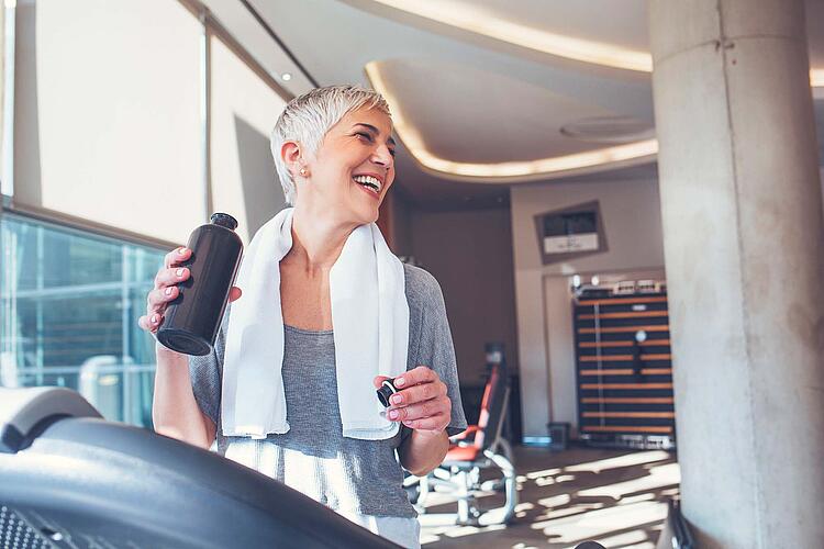 Frau im Fitnessstudio trinkt während einer Trainingspause Wasser.