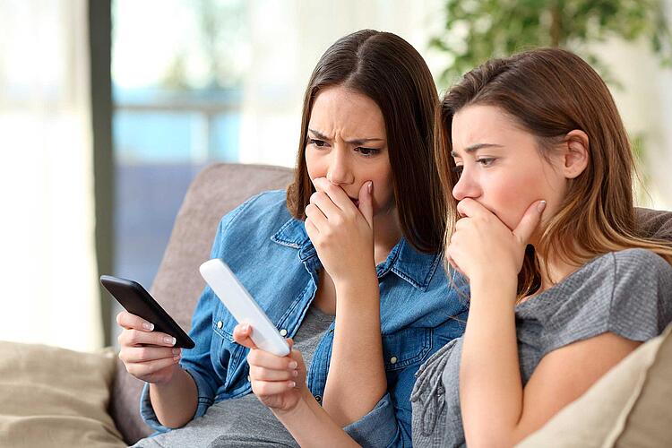 Zwei junge Frauen schauen besorgt auf ihre Smartphones.