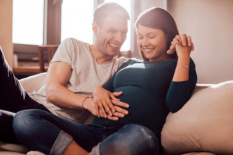 Mann legt die Hand auf den Bauch seiner schwangeren Partnerin.