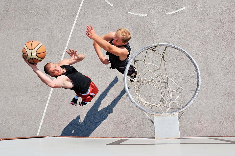 Zwei Männer werfen mit einem Basketball auf einen Korb.