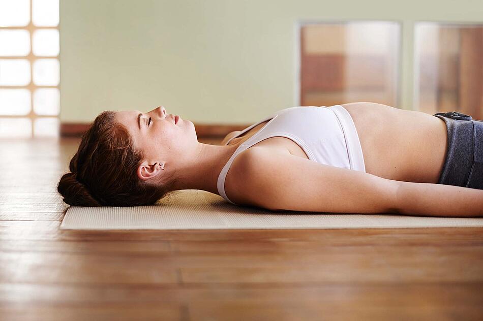 Junge Frau liegt in Sporttop mit geschlossenen Augen auf einer Matte in einem Studio. – Bild: istockphoto.com / TE YAPR - Bildnachweis: © istockphoto.com / TE YAPR Junge Frau liegt in Sporttop mit geschlossenen Augen auf einer Matte in einem Studio.