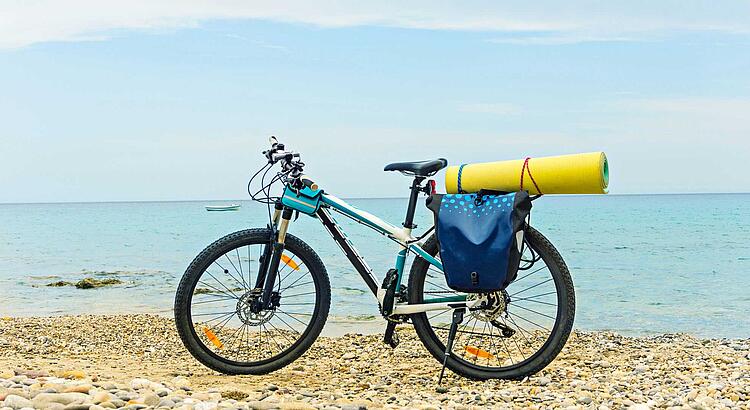 Fahrrad mit Packtaschen und Isomatte auf dem Gepäckträger steht am Meer.