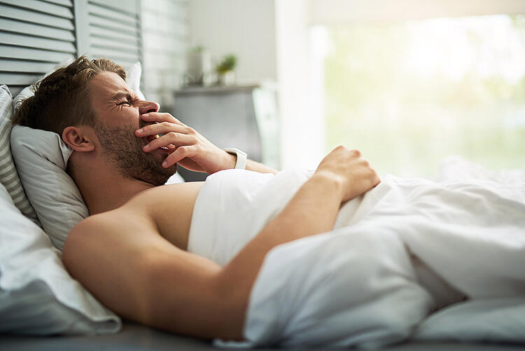 Mann liegt im Bett und gähnt