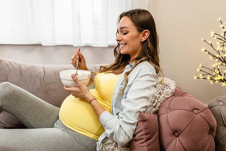 Schwangere isst gemütlich auf dem Sofa