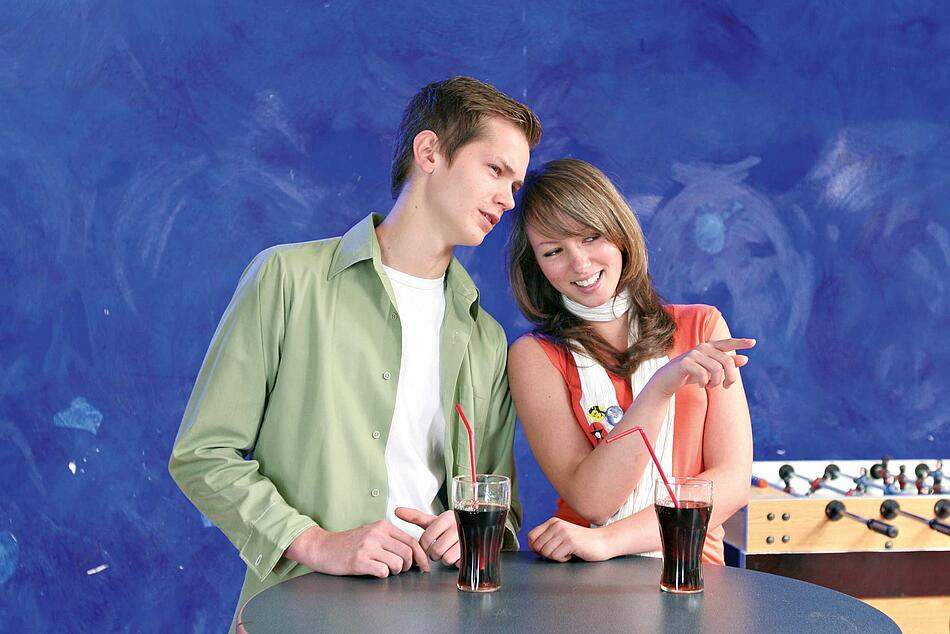 Junges Paar steht an einem Stehtisch auf dem Getränke stehen.