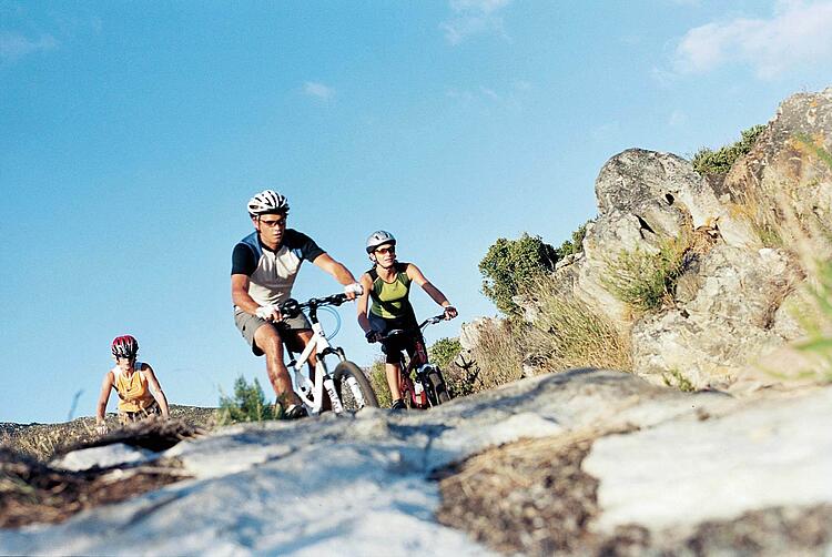 Gruppe junger Leute fährt Mountainbike in felsigem Gelände.