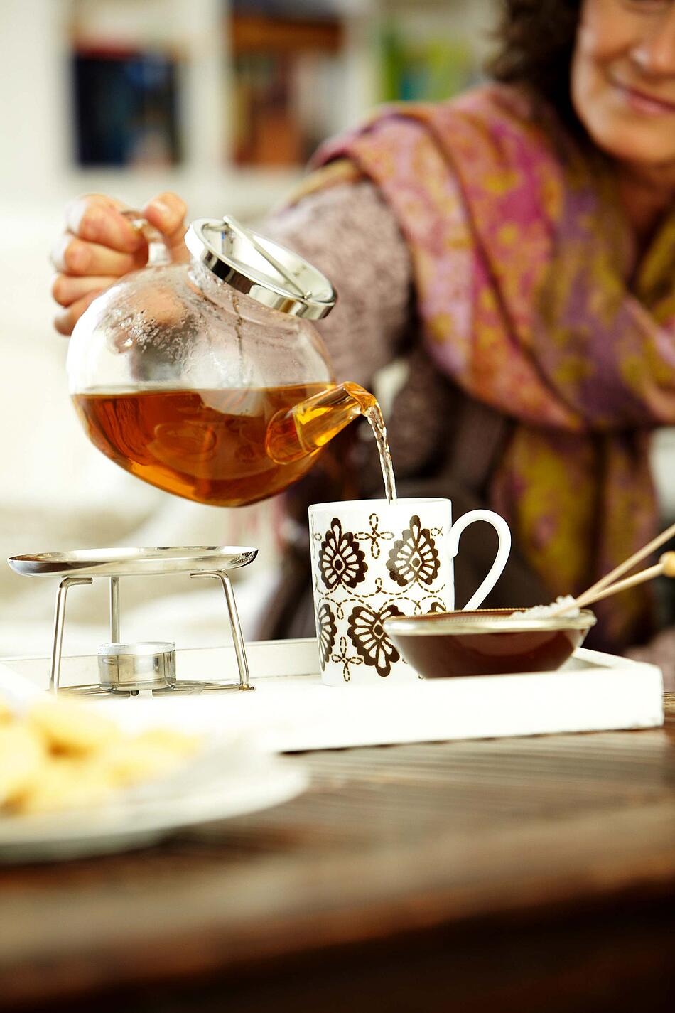 Frau gießt Tee in eine Tasse.