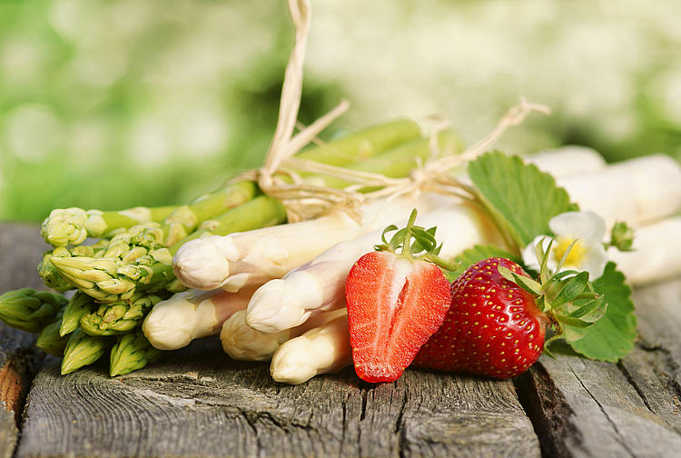 Grüner und weißer Spargel auf einem Holztisch davor zwei Erdbeeren.