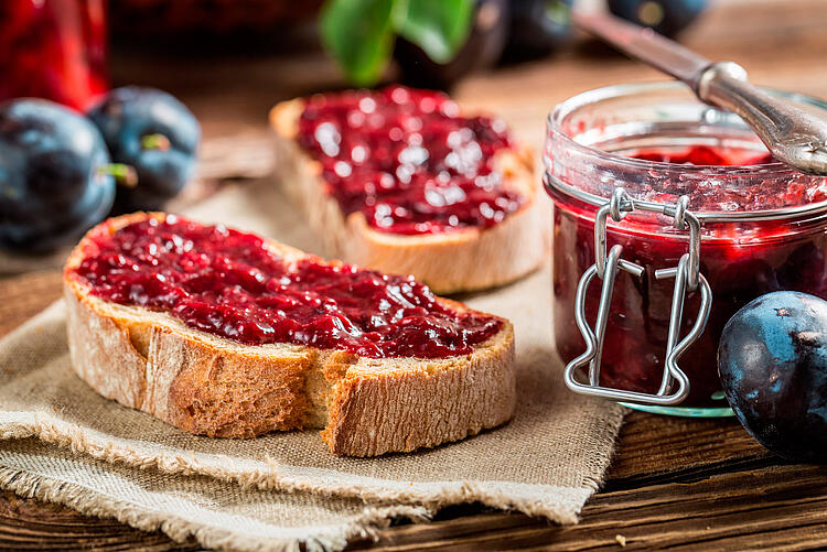 Zwei Scheiben Baguette mit Pflaumenmus, daneben Einmachglas mit Marmelade. 