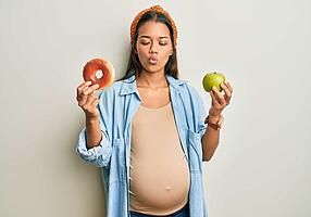 Ernährung in der Schwangerschaft:  Schwangere hält einen Apfel in der einen Hand und einen Bagel in der anderen Hand