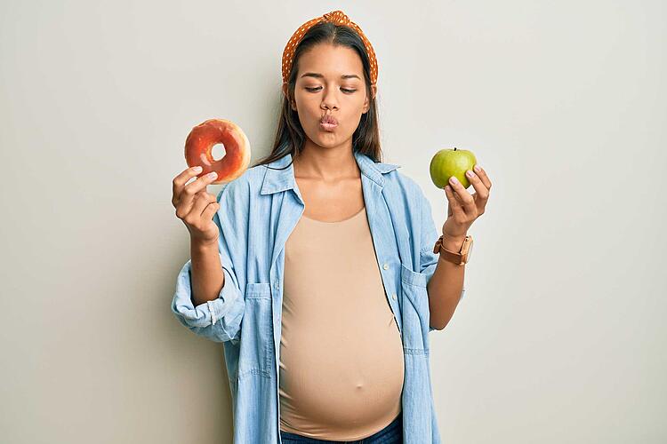 Ernährung in der Schwangerschaft:  Schwangere hält einen Apfel in der einen Hand und einen Bagel in der anderen Hand