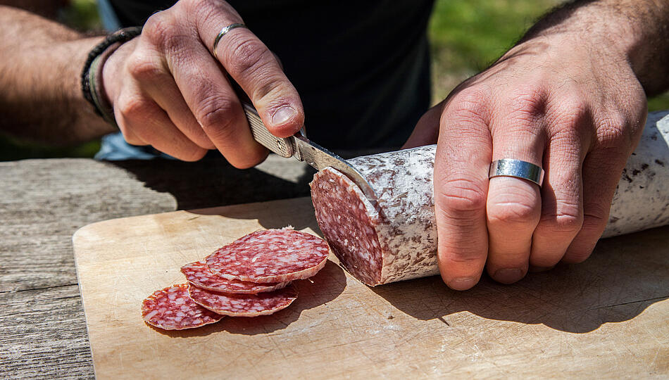 Mann schneidet Salamiwurst auf Holzbrett