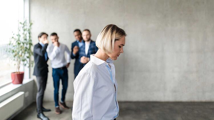 Gruppe Männer flüstert hinter dem Rücken einer Kollegin