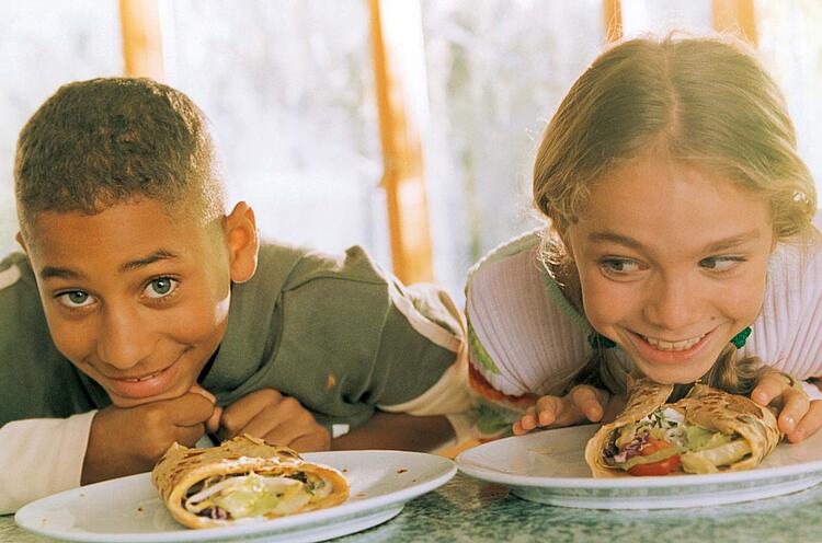 Lachende Kinder vor Tellern mit Wraps.