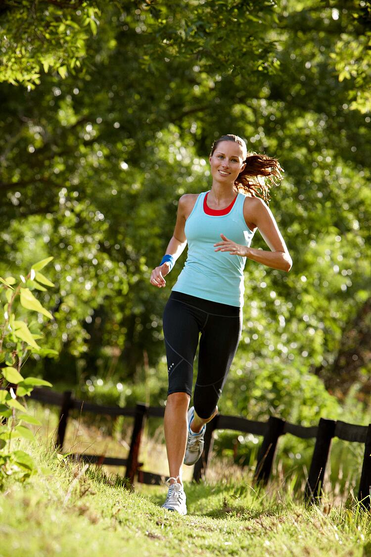 Junge Frau in Laufkleidung beim Joggen auf einem Weg neben einem Holzgeländer.