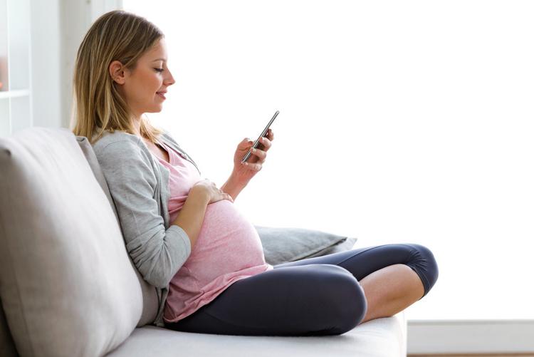 Schwangere sitzt auf dem Sofa und schaut auf ihr Smartphone