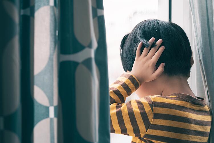 Junge schaut aus dem Fenster und hält sich die Ohren zu