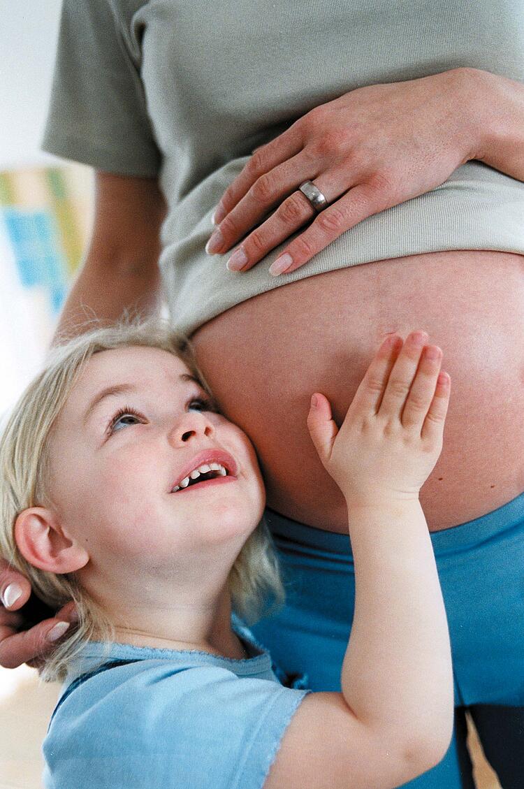 Kleines Mädchen streichelt den Bauch einer Schwangeren.