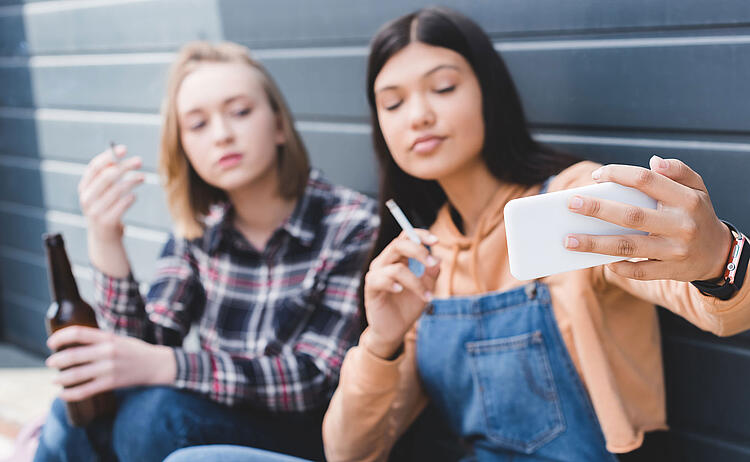 Zwei junge Frauen machen ein Selfie mit Zigarette und Bierflasche in der Hand