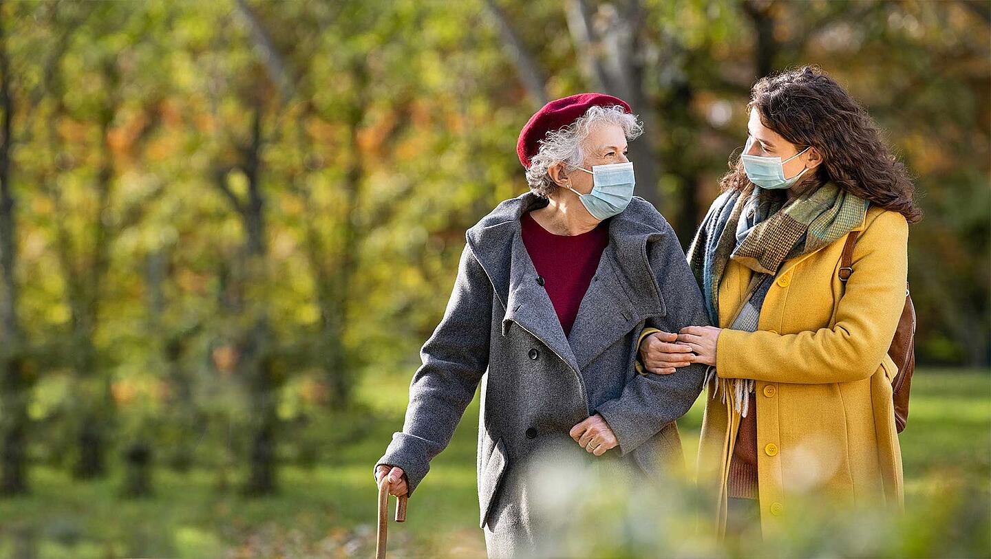 Zwei Frauen gehen mit Maske im Park spazieren