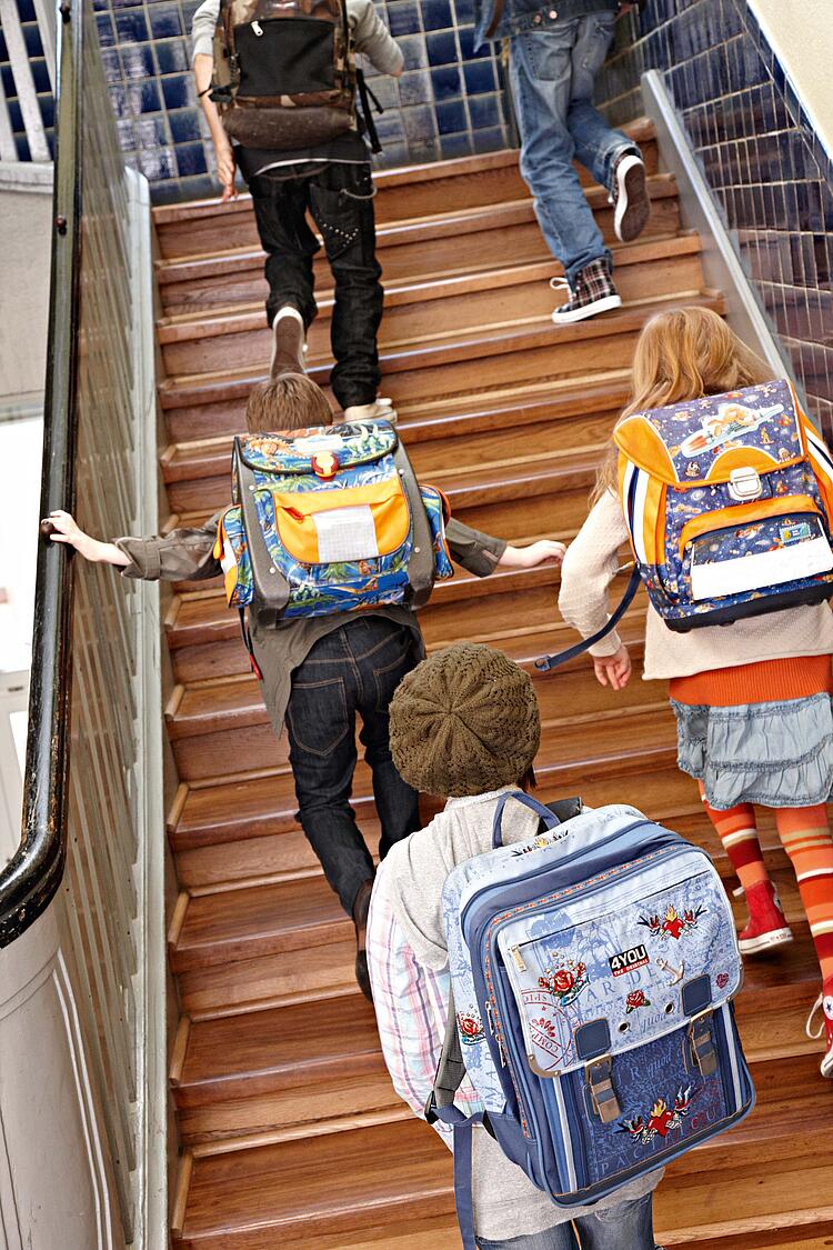Grundschulkinder mit Ranzen auf dem Rücken laufen eine Treppe hoch.