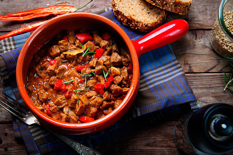 Eintopf mit Fleisch und rotem Gemüse in roter Stielkasserole.