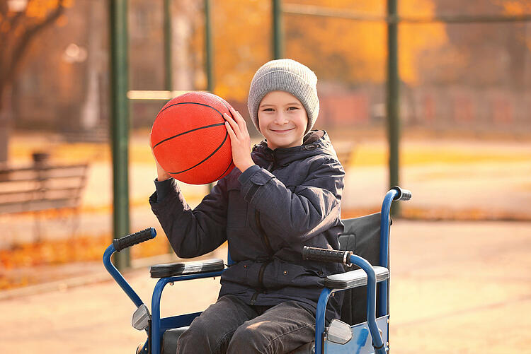 Junge im Rollstuhl spielt Bastketball.