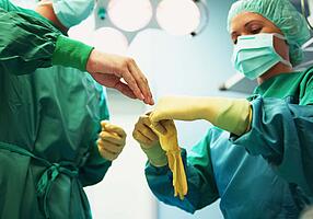 Ärzte in OP-Kleidung ziehen sich die sterilen Handschuhe an.