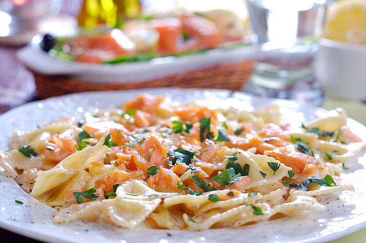 Pastasalat mit Lachs angerichtet auf einem Teller.