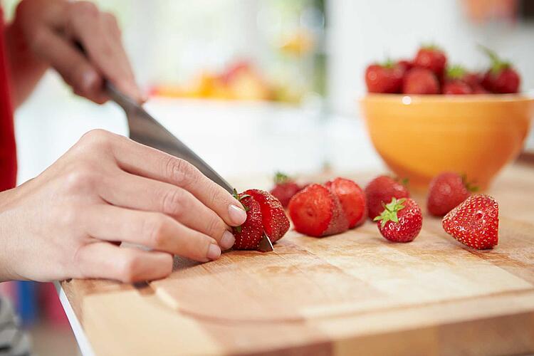 Hände schneiden Erdbeeren