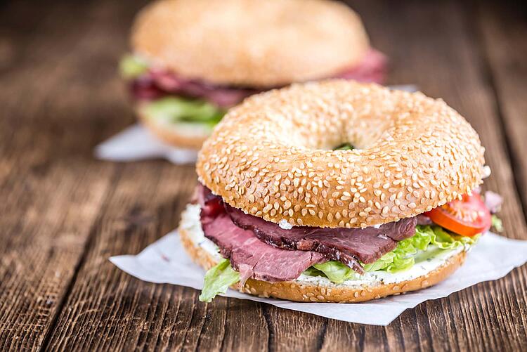 Bagel mit Roastbeef und Salat liegt auf einer Serviette auf einem Holztisch.